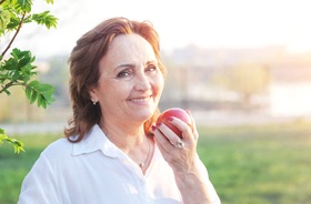Woman enjoying apple with the help of her implant dentures