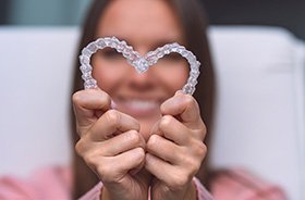 Smiling woman holding Invisalign aligners in heart shape