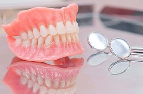 Full set of dentures next to dental mirrors
