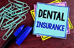 Dental insurance written on blue sticky note next to paperclips