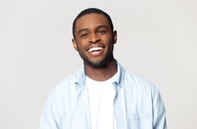 Man in white shirt standing and smiling against gray background