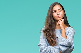 Woman in blue sweater thinking, has questions about emergency dentistry