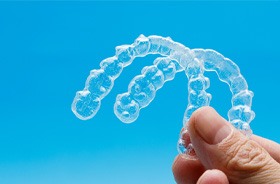 Gloved hand holding two clear aligners against blue background