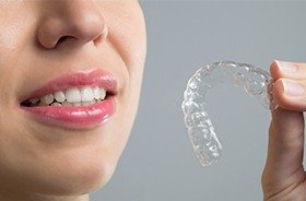 Closeup of smile and hand holding Invisalign tray