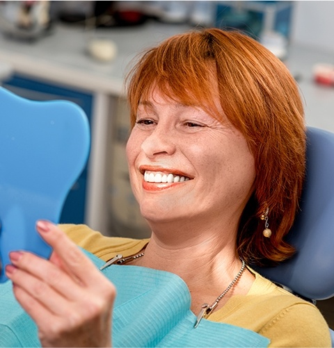 Older woman in dental chair looking at her smile in mirror