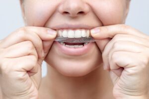 Woman placing whitening strip on her top teeth