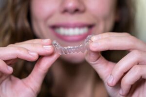 Smiling woman holding Invisalign aligner 