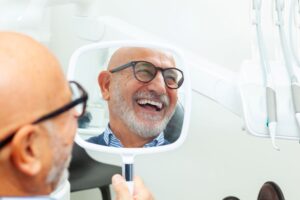 Smiling senior dental patient reflected in hand mirror 